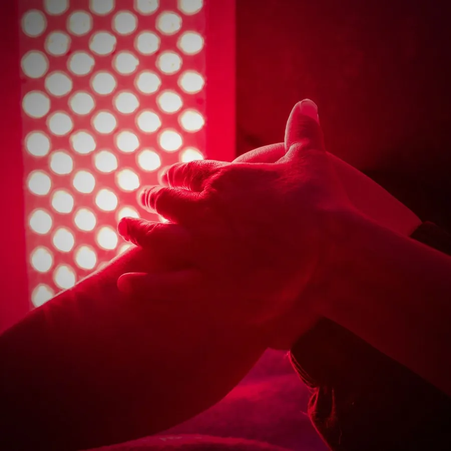 Hands resting in front of a glowing red light therapy panel
